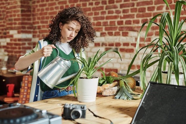 Woman watering plants with recycled water from a container, showing a sustainable practice for water conservation in a residential setting.