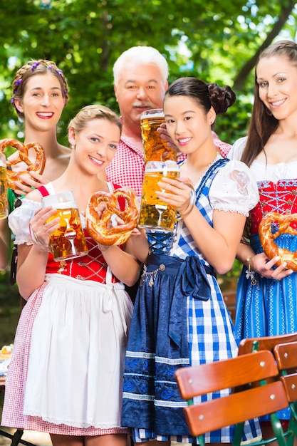 A group of people dressed in traditional German costumes, raising beer steins in a festive atmosphere during Oktoberfest in Blumenau, Brazil.