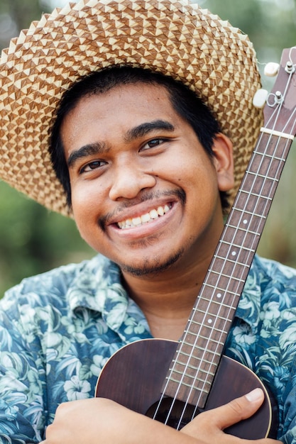 A close-up shot of a young Brazilian musician, with a bright smile, playing a traditional Brazilian instrument (like a cavaquinho or berimbau) in a modern recording studio. The studio equipment is visible in the background, highlighting the blend of traditional Brazilian sounds with modern production techniques.