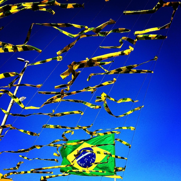 A panoramic view of a large open-air music festival, with a Brazilian flag waving prominently in the foreground. The stage is set with vibrant lights and visuals, and a popular Brazilian band is performing, drawing a huge crowd of international fans.