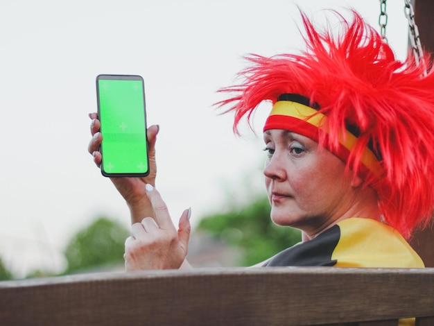A close-up shot of a person using a mobile app at the Rio Carnival, showing the carnival schedule, maps, and event information on the screen. The background blurs the vibrant street scene during the festival.