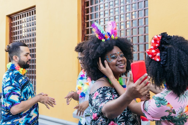 A diverse crowd of people celebrating at a Brazilian carnival street party, holding up their smartphones to capture the moment. The background features colorful decorations and vibrant street life.