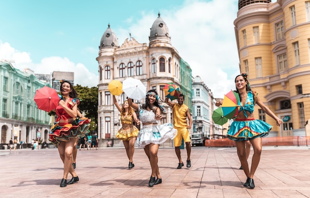 A group of dancers performing Frevo in the streets of Recife, Pernambuco, dressed in traditional colorful costumes and holding small umbrellas.