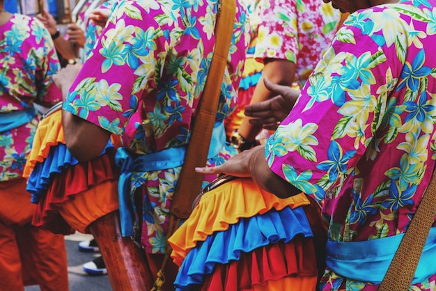 A colorful photograph depicting dancers in traditional Caboclinha costumes performing in the streets of Pernambuco, showcasing their indigenous attire and symbolic weapons in a festive setting.