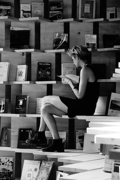 A black and white photograph of Machado de Assis, looking thoughtful, in a library setting with shelves filled with books.