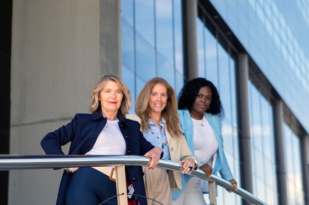 A group of Brazilian women in business attire, standing together in front of a modern office building, smiling and looking confident.