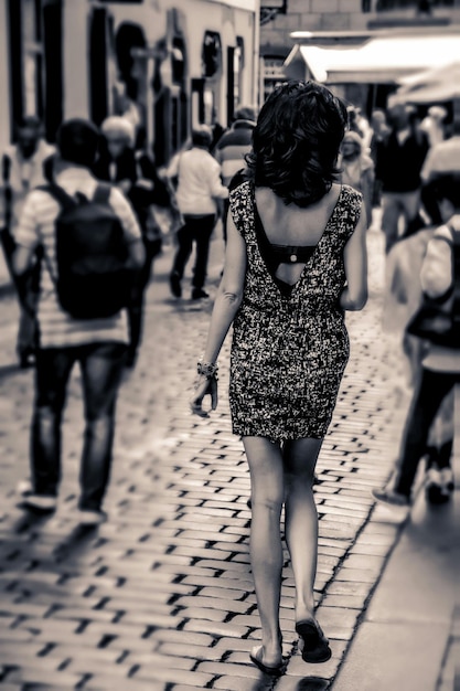 A black and white photograph of a young Brazilian musician busking in a crowded street. He is playing an acoustic guitar and singing with enthusiasm, while people walk by, some stopping to listen or drop money into his case.