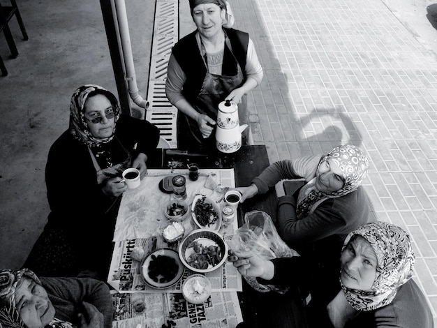 A black and white photo showing a group of Brazilian intellectuals gathered around a table, engrossed in a deep discussion. The atmosphere is scholarly and intense, with books and papers scattered around, reflecting their dedication to intellectual pursuits and their influence on Brazilian society.