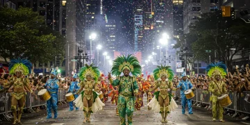Dançarinos de samba em trajes coloridos celebrando o Carnaval Brasileiro em uma rua movimentada dos EUA, com a multidão eufórica ao redor.